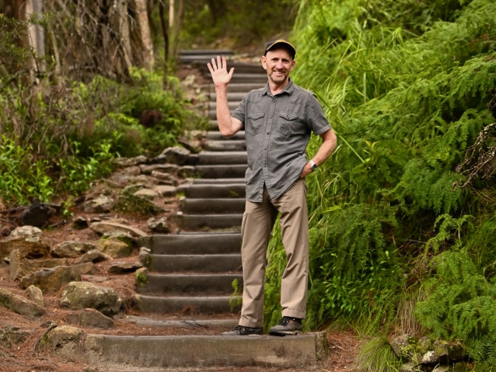 Hiker on a trail in the Blue Mountains National Park with scenic views of cliffs and valleys.