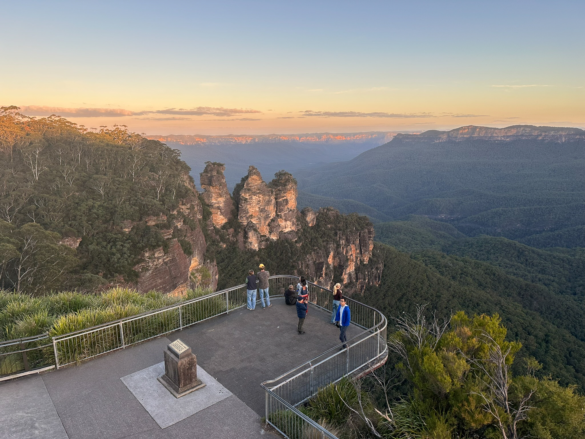 Early morning sunrise over the iconic Three Sisters rock formation in Katoomba, with soft golden light illuminating the Blue Mountains.